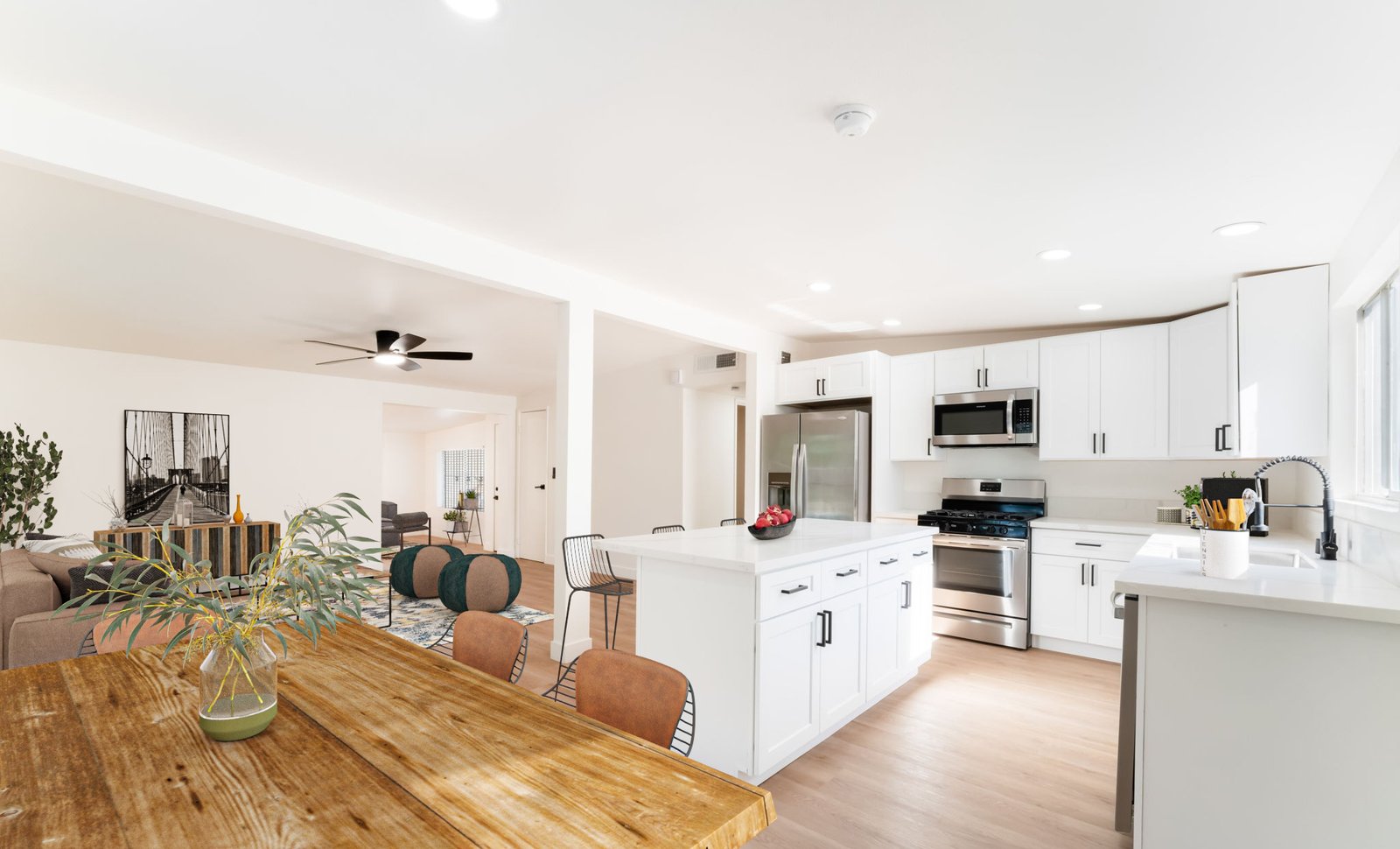 Bright modern kitchen with white cabinets, stainless steel appliances, and a wooden dining table.