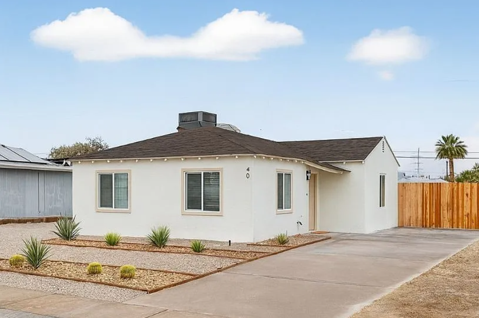 Single-story white house with a dark roof, front yard landscaping, and a concrete driveway.