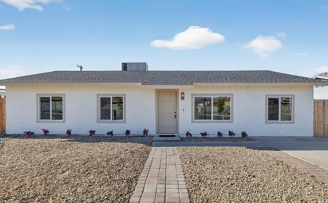 Single-story white residential home with a front door and multiple windows, surrounded by gravel landscaping.