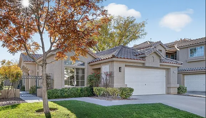 Single-story residential house with a garage and landscaped front yard featuring a tree and shrubs.