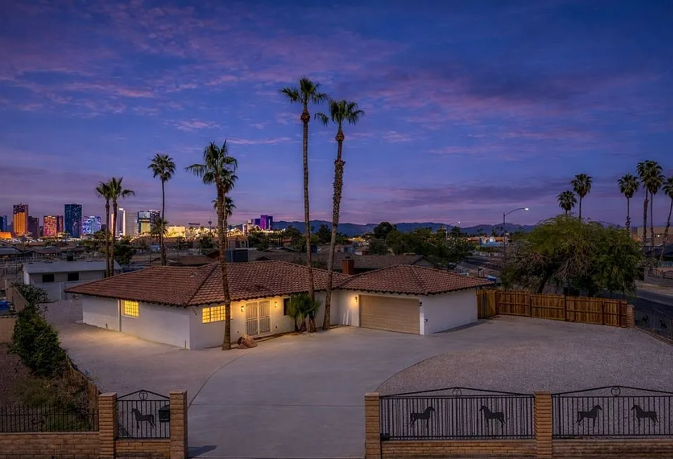 Warm-lit remodeled home exterior at 1486 Rawhide St, Las Vegas, NV, under a dusk sky with palm trees and a red tile roof.